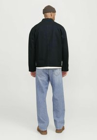 Zwarte spijkerjack met een relaxte fit, gecombineerd met lichtblauwe baggy jeans. De outfit heeft een minimalistisch ontwerp en een effen kleurenschema.