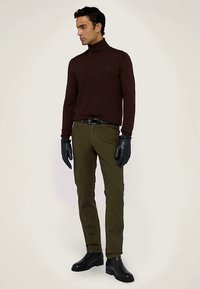 Dunkelroter Rollkragenpullover, olivgrüne Hose, schwarze Handschuhe und schwarze Stiefeletten, getragen von einem männlichen Model vor neutralem Hintergrund.