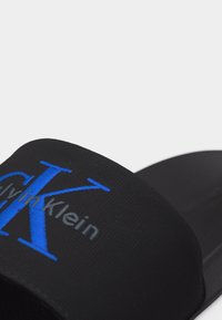 Μαύρο σανδάλι με λουράκι και κεντημένο λογότυπο Calvin Klein σε μπλε και γκρι χρώμα.
