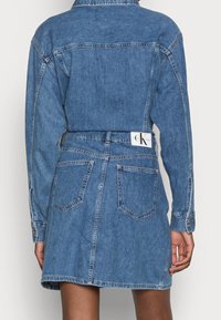 Jeansklänning med ljusblå tvättning, krage, långa ärmar och bälte i midjan. Har två bakfickor och märkesetikett.