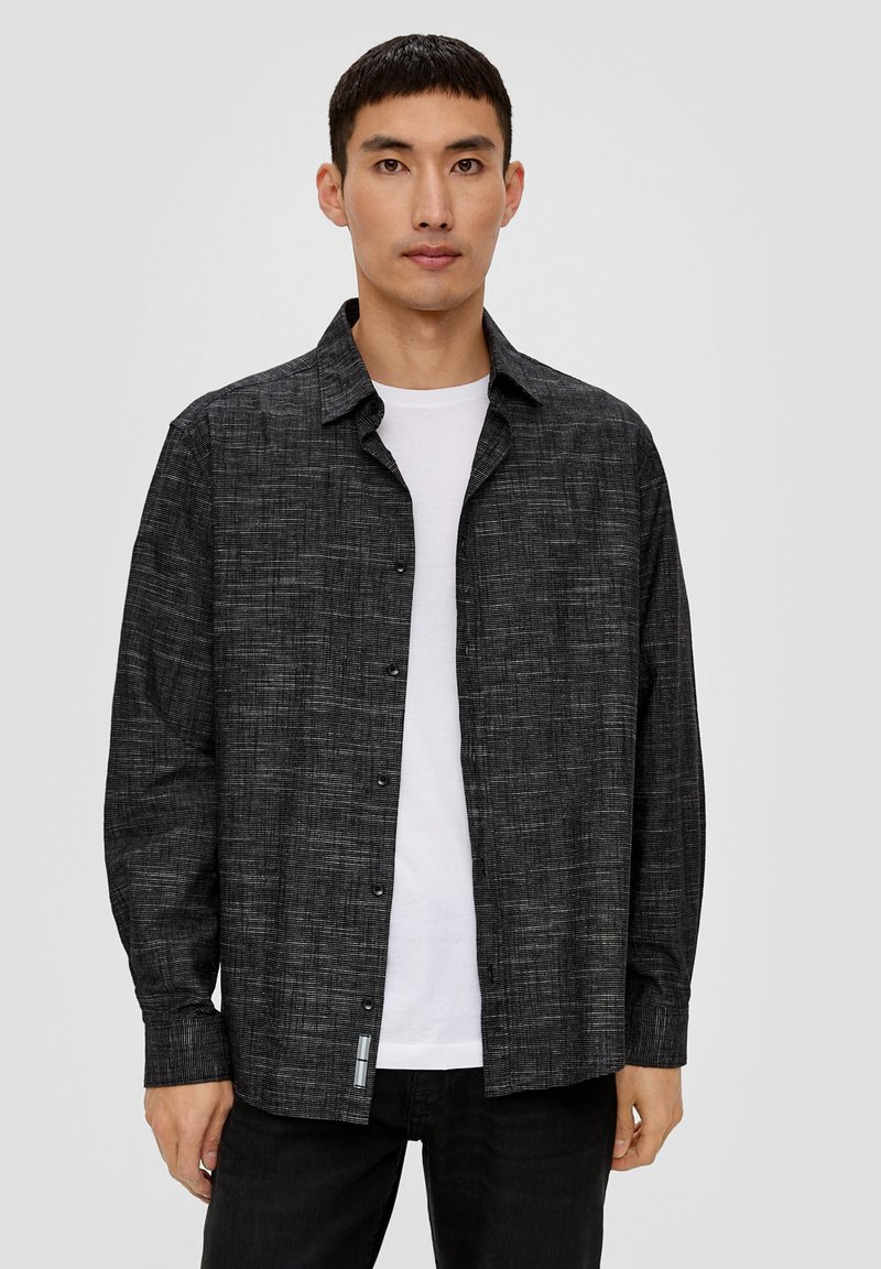 Zwarte gebloemde button-up shirt met een relaxte pasvorm, gemaakt van geweven stof. Het heeft lange mouwen en een klassieke kraag, gedragen over een wit t-shirt.