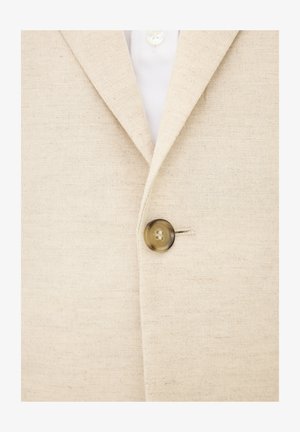 Beige linnen blazer met een gestructureerde afwerking, voorzien van een enkele bruine knoopsluiting en een klassieke reverskraag. Witte blouse eronder.