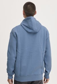 Sudadera de algodón azul con capucha ajustable y cordón, puños y dobladillo acanalados. Textura suave, corte relajado y sin patrones visibles.