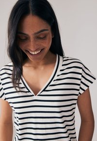 V-ringad T-shirt med ränder i vitt och svart, med korta ärmar och ett mjukt, texturerat tyg med horisontella ränder.