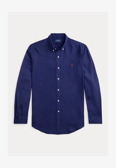 Camisa de lino azul marino de manga larga con cuello abotonado. Presenta un logo bordado en rojo en el lado izquierdo del pecho y botones blancos.