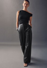 Zwart top met één schouder, gecombineerd met hooggetailleerde zwarte leren broek met een getailleerde pasvorm en zijzakken. Glad oppervlak met een gestroomlijnd ontwerp.