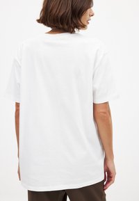White cotton t-shirt featuring a relaxed fit, short sleeves, ribbed crew neck, and a smooth texture with no visible patterns or graphics.