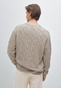 Beiger, grob gestrickter Pullover mit entspannter Passform, versehen mit strukturierten Mustern und gerippten Bündchen sowie Saum. Kombiniert mit hellen Hosen.