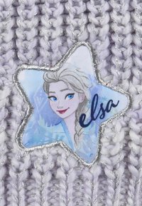 Tessuto lavorato a maglia lavanda con accenti argentati presenta una toppa a forma di stella blu che raffigura un personaggio, etichettato "elsa" in corsivo nero.