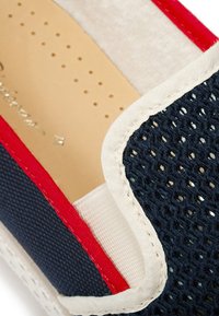 Marineblauwe canvas instap schoenen met een geweven mesh ontwerp, witte voering en rode accenten rond de opening. Geïntegreerde textuur aan de binnenkant voor comfort.