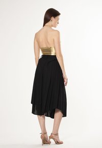 Falda asimétrica negra combinada con un top sin tirantes brillante en dorado. Textura suave, diseño ajustado en el torso, con un drapeado fluido.