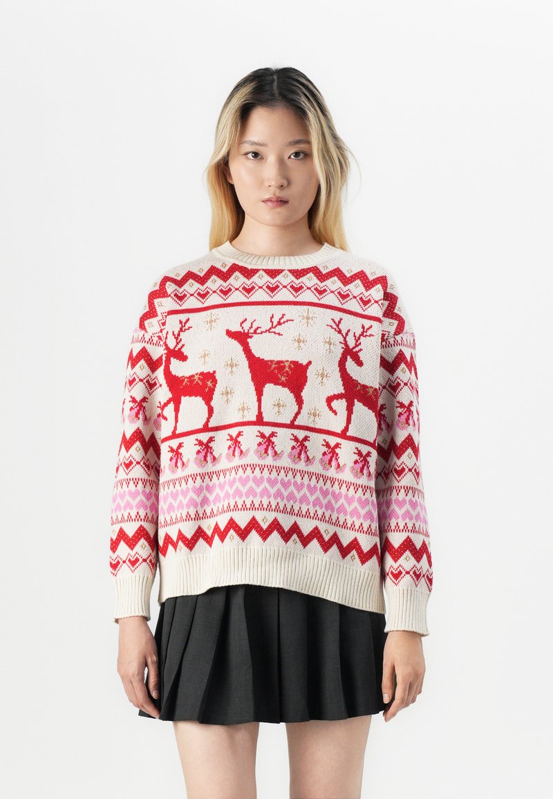 Κόκκινο και κρεμ πουλόβερ με μοτίβα από ταράνδους, σχέδια ζιγκ-ζαγκ και καρδιές. Ριμπ μανσέτες και στρίφωμα, με χαλαρή εφαρμογή.