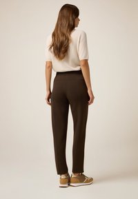 Brązowe spodnie sportowe z elastycznym paskiem w talii, w połączeniu z beżowymi i złotymi trampkami. Góra jest jasna i krótki rękaw.