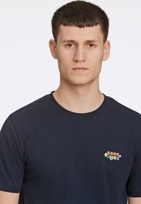 Camiseta de algodón azul marino con escote redondo y mangas cortas, que presenta el texto bordado multicolor "GOOD VIBES" en el lado izquierdo del pecho.