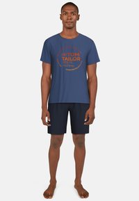 Camiseta de algodón azul marino con gráfico circular en naranja, mostrando el nombre de la marca "TOM TAILOR" y texto. Combinada con pantalones cortos azul marino.