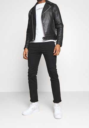 Sort motorcykeljakke i læder med sølvfarvede lynlåse, kombineret med en hvid t-shirt og sorte skinny jeans. Fuldført med hvide sneakers.