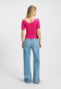 Rosa ribbad topp med korta ärmar och V-ringning, kombinerad med högmidjade ljusblå vida jeans. Bakifrån syns detaljerna på banden.