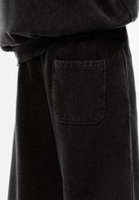 Čierne bavlnené tepláky s bočnou vreckom, s mäkkou textúrou a voľným strihom. Pás je elastický, čo zabezpečuje pohodlie.