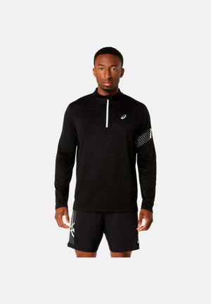 Uomo che indossa una maglia sportiva nera a maniche lunghe con cerniera parziale e pantaloncini neri abbinati con motivi a puntini bianchi su manica e gamba.