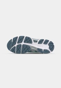 Semelle extérieure d’une chaussure de course avec motifs en caoutchouc gris pour la traction et semelle intermédiaire blanche, présentée sur un fond gris clair uni.