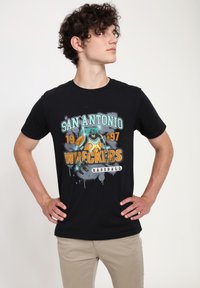 Černé tričko s krátkým rukávem zdobené barevným grafickým designem s textem "San Antonio Wreckers Baseball" a ilustrovanou postavičkou.