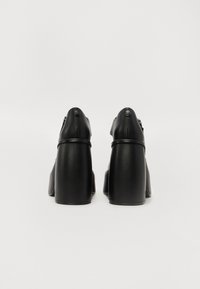 Mustad musta nahast kõrged jalatsid, millel on sile tekstuur, ümarad tipud ja lai plokknina. Disain sisaldab peeneid õmblusi ja metallaktsente.