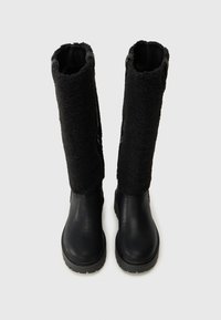 Botas negras hasta la rodilla con una parte inferior de cuero y una parte superior de textura suave. Suela de goma duradera con un patrón de relieve para mayor tracción.