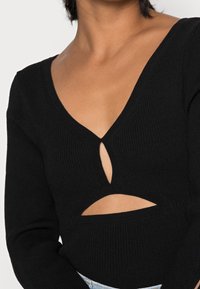 Haut noir à manches longues côtelé avec un décolleté en V profond et des découpes au niveau de la poitrine et de la taille. Texture douce avec une silhouette ajustée.