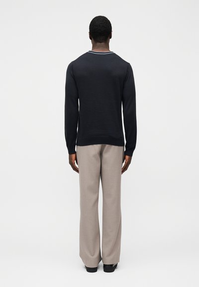 Pull bleu marine à col rond avec surpiqûres blanches en accent, associé à un pantalon large gris clair en tissu texturé.