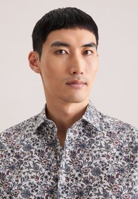 Biała koszula na guziki z kwiatowym wzorem, zdobiona wielobarwnymi kwiatami. Koszula z kołnierzykiem, dopasowanym krojem i krótkimi rękawami.