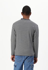 Langermet skjorte med svart-hvitt stripemønster, rund halslinning og mykt stoff. Kombinert med blå cargo-bukser.