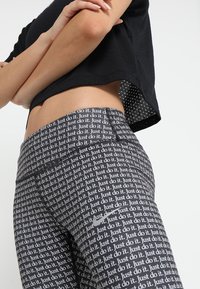 Czarne legginsy z powtarzającym się białym napisem "Just do it". Wysoki stan, elastyczny materiał o gładkiej fakturze.