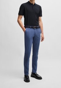 Polo noir, pantalon bleu clair, ceinture tissée marine et chaussures noires. Le polo a un col ; le pantalon a des poches latérales et une coupe ajustée.