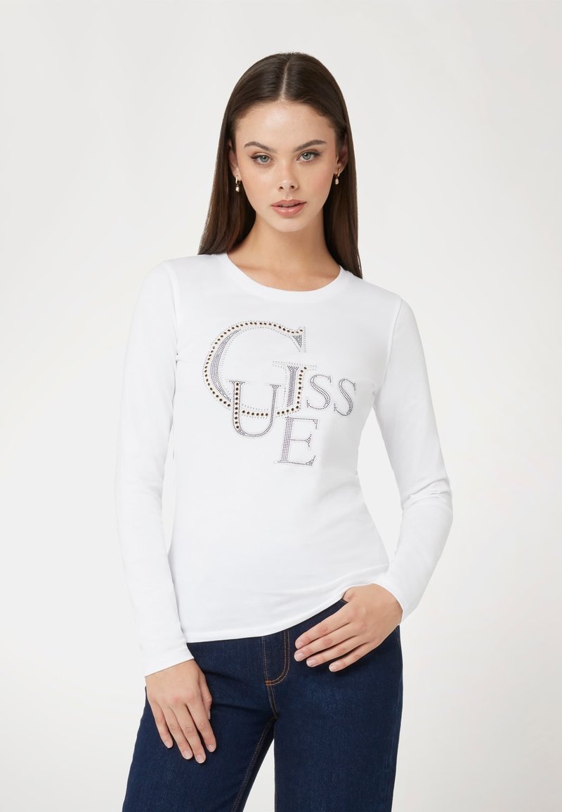 Baltas ilgomis rankovėmis marškinėliai su dideliu logotipu "GUESS", papuoštu kristalais. Minkšta medvilnės medžiaga su prigludusia siluetu.