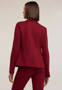 Blazer tailored bordeaux con un design strutturato, maniche lunghe e una texture liscia. Presenta un dorso ventilato e un taglio moderno.