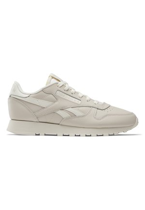 Beżowy niski sneaker Reebok z białymi sznurowadłami, logo z boku i na pięcie oraz płaską gumową podeszwą.
