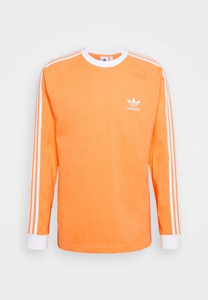 Sudadera Adidas naranja de manga larga con cuello redondo blanco, puños, tres rayas blancas en las mangas y logo de Adidas en el pecho.