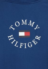 Felpa blu con un logo circolare "TOMMY HILFIGER" e un design rettangolare della bandiera rossa, bianca e nera al centro.