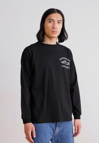 Long-sleeve black T-shirt with graphic text and fish design on the chest. Made from soft fabric, paired with blue jeans.