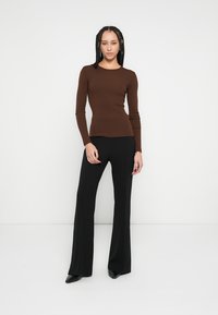 Top marrone a maniche lunghe con costine abbinato a pantaloni neri svasati. L'outfit presenta un design aderente con una texture liscia e una silhouette elegante.