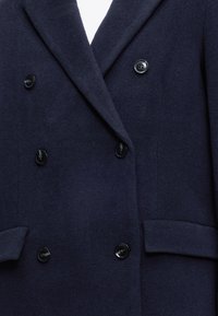 Manteau en laine bleu marine à double boutonnage avec boutons noirs et revers en encoche, doté de deux poches avant à rabat.