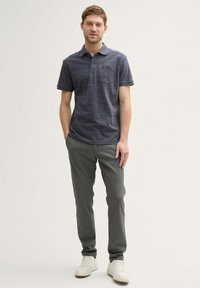 Granatowa koszula polo z subtelnymi poziomymi paskami, z kieszonką i krótkimi rękawami; zestawiona z jasnoszarymi spodniami i białymi trampkami.