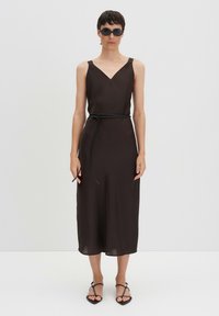Abito marrone senza maniche con scollo a V e una cintura nera. Tessuto liscio, lunghezza al ginocchio, abbinato a sandali neri con cinturini e occhiali da sole.