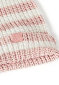 Pletená deka v růžovém a bílém pruhovaném vzoru s texturovaným povrchem. Na okraji je přišitá nášivka s logem. Měkký a útulný materiál.
