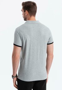 Grijze polo met korte mouwen en een zwarte rand op de kraag en mouwen. Zachte stof met een gladde textuur, met een rechte zoom.