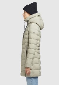 Lys grå pufferjakke med hætte, udstyret med vandrette syninger, sidelommer og justerbare snore. Sammen med en sort strikket beanie.