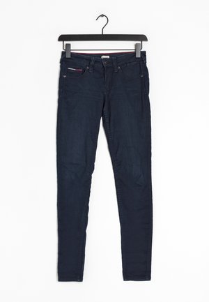 Ciemnoniebieskie jeansy slim fit z pięcioma kieszeniami, zapięciem na guziki i szlufkami na pasek, wiszące na czarnym wieszaku na białym tle.