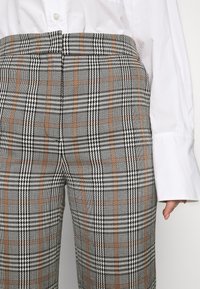 Rutig byxor i grått, svart och brunt. Materialet har en strukturerad väv med hundtandsmönster och rutiga mönster. Öppen midja.