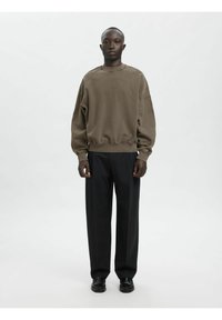 Olivzaļš oversize stils džemperis ar ribotiem aproču un apakšmalas galiem, kopā ar melnām platu kāju biksēm, kas izceļas ar teksturētu audumu un vienkāršu dizainu.