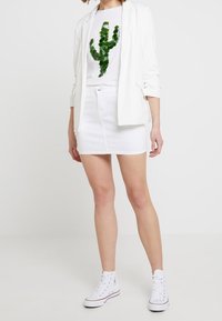 White fitted blazer, white t-shirt with green cactus design, white denim skirt, and white high-top sneakers. Smooth fabric, casual look.